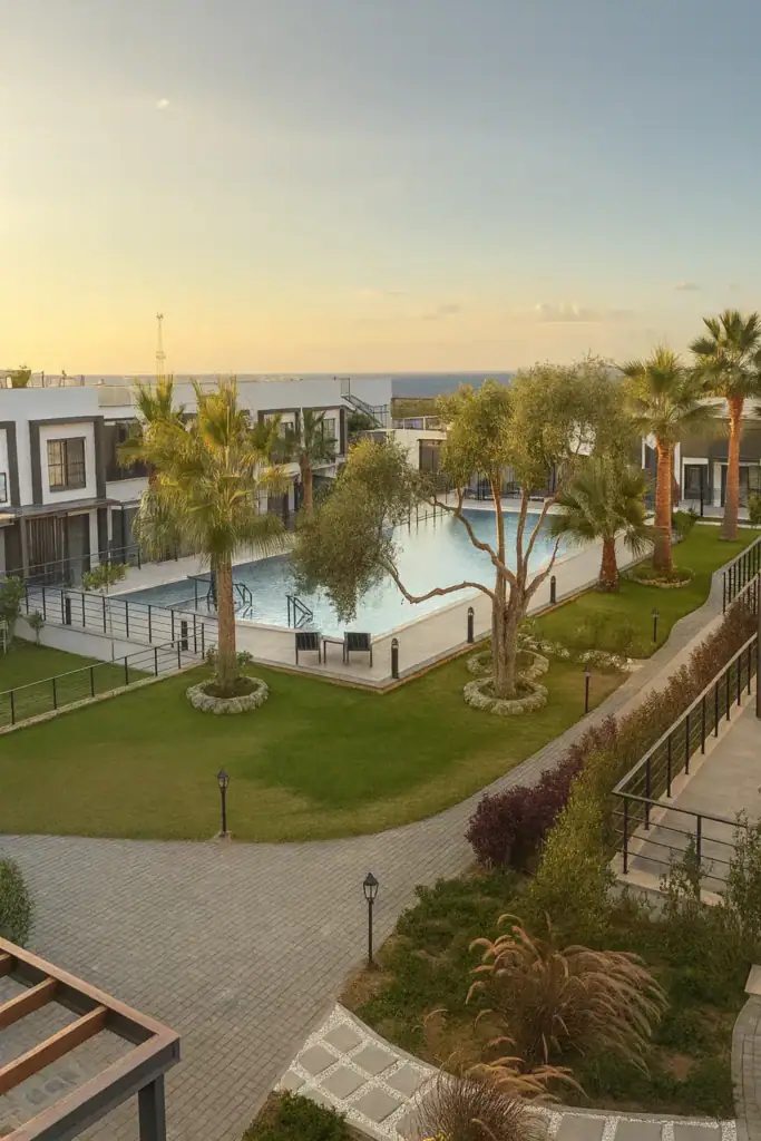 A view of a luxurious residential development in North Cyprus featuring a swimming pool, palm trees, and well-maintained gard.