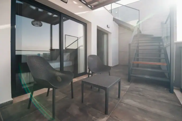Modern balcony with glass railing, outdoor seating, and stairs leading to upper level in a contemporary property in North Cyp.
