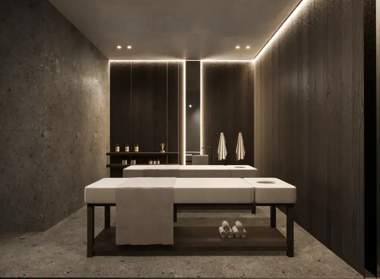 Luxurious modern spa treatment room with two massage tables, dark wood paneling, stone walls, and warm ambient lighting.