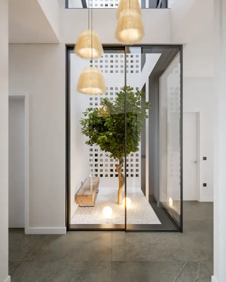Indoor courtyard featuring a vibrant green tree, contemporary lighting, and minimalist design elements.