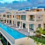 Luxurious modern apartment complex with a large swimming pool in North Cyprus, surrounded by scenic mountains and lush greene.