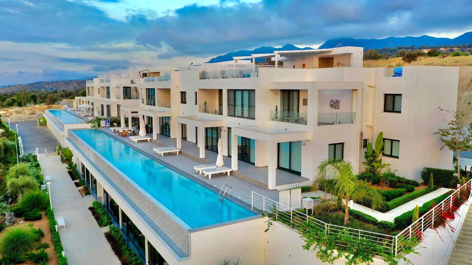 Luxurious modern apartment complex with a large swimming pool in North Cyprus, surrounded by scenic mountains and lush greene.